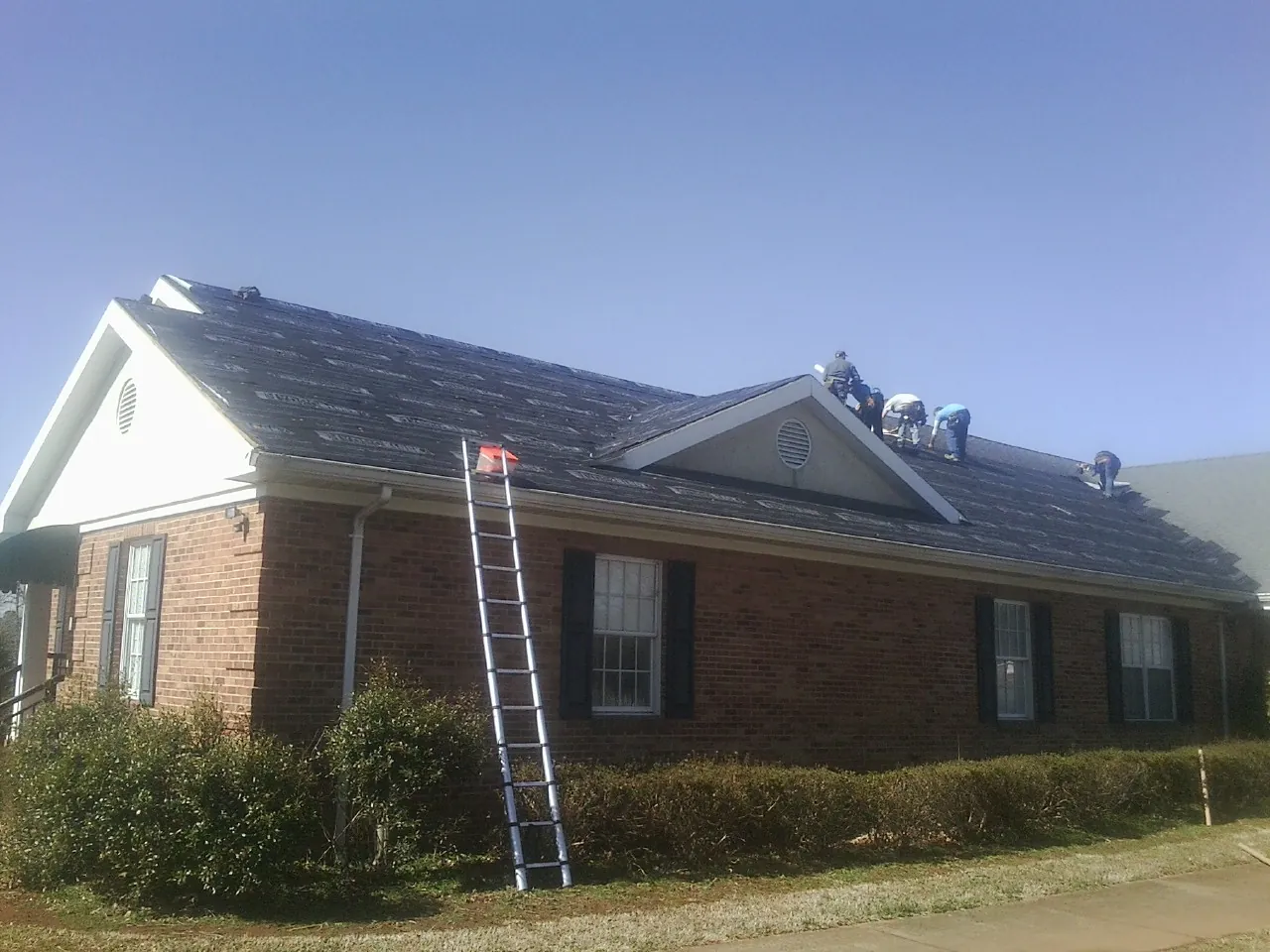 Crew tearing shingles off a brick ranch roof with a ladder set — Emergency Roof Repair work by our crew in Mayport