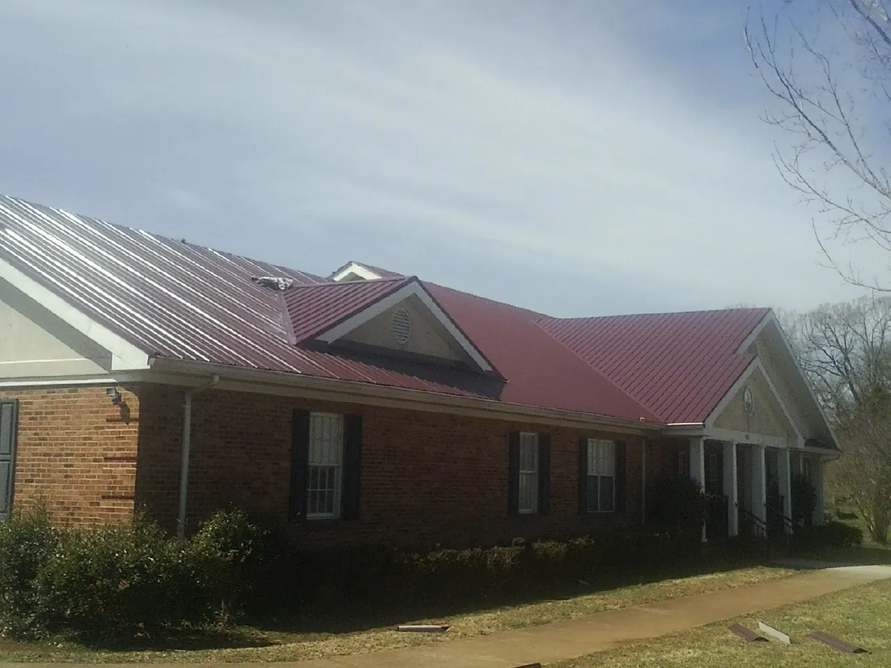 Red metal roof with gabled entries on a long brick building, from a Hail Damage Roof Repair job in Mayport