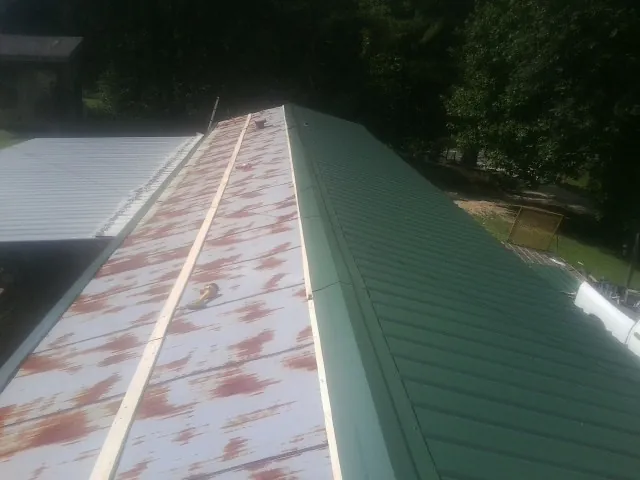 Old rusted panels beside newly installed green metal roofing — Wind Damage Roof Repair by Roofing Brothers in Mayport