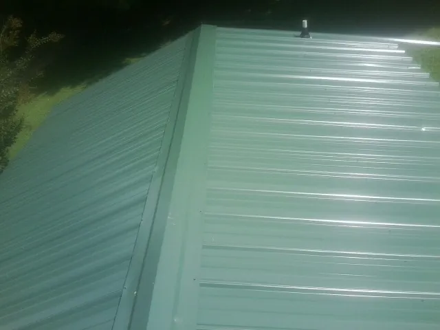 New green metal panels meeting at the ridge of a roof — Flat Roof Repair work by our crew in Mayport