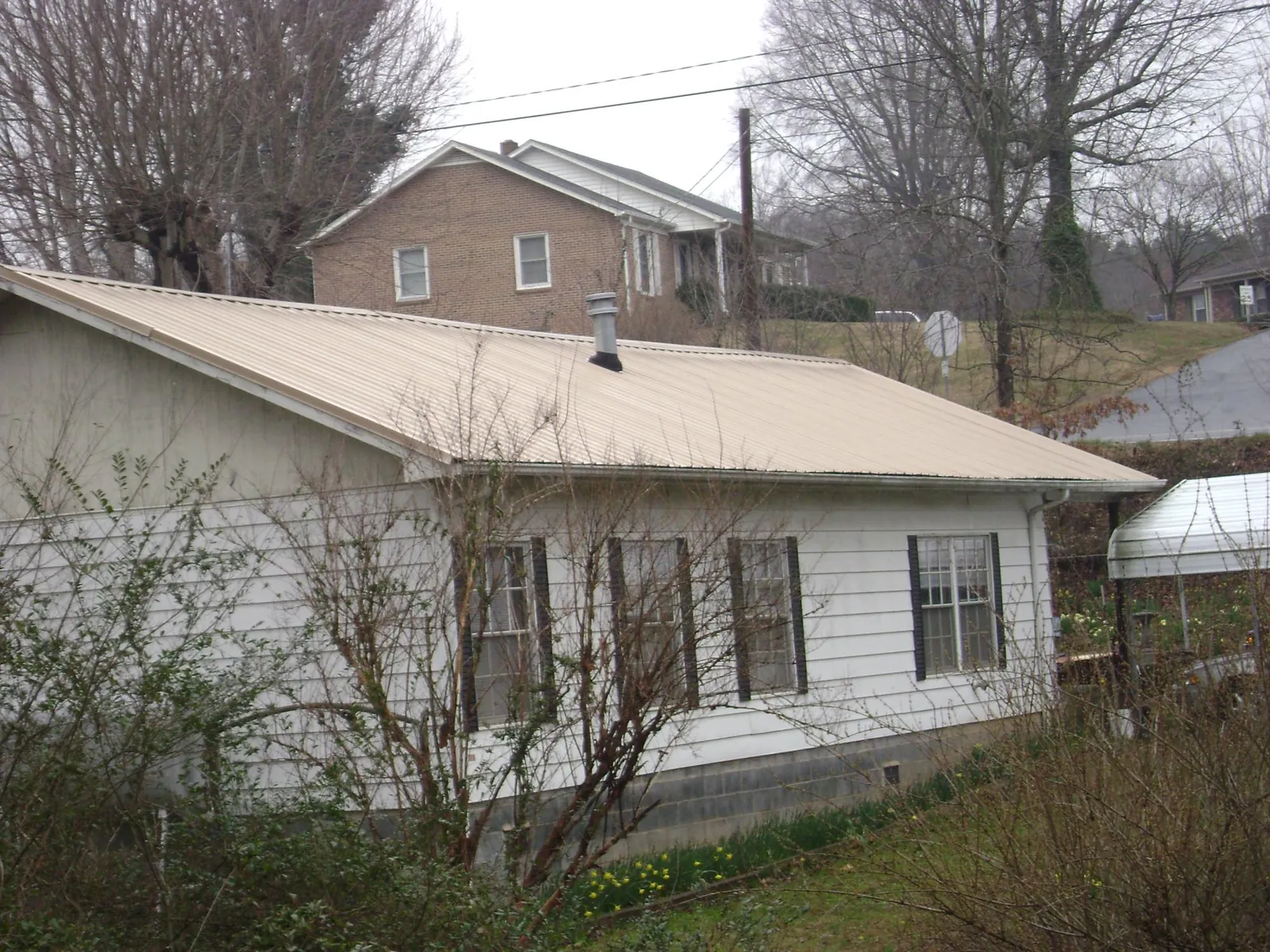 Tan metal roof on a white sided house set into a hillside — Commercial Roofing by Roofing Brothers in Mayport